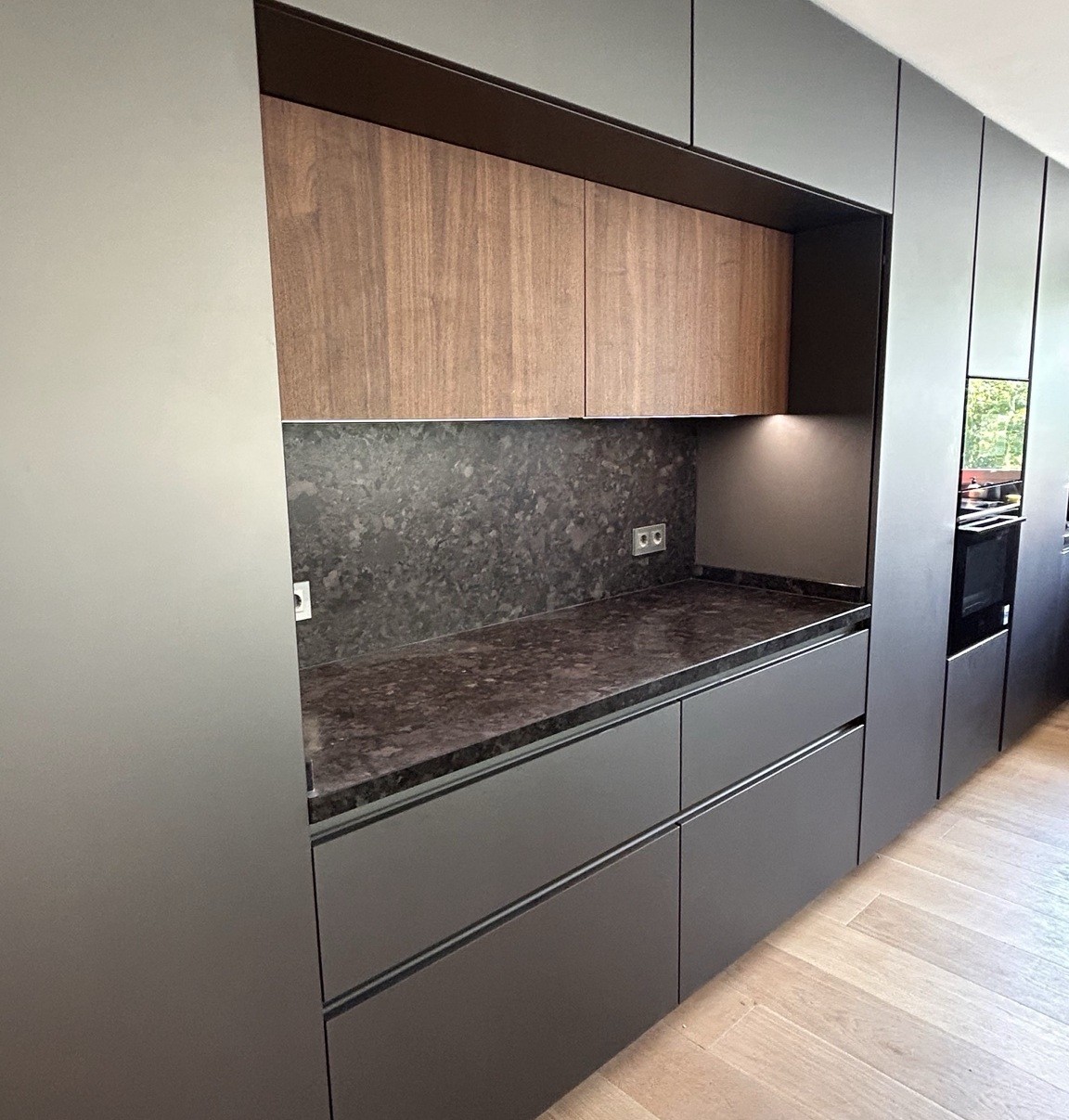 Cocina lineal con mobiliario gris, madera natural e iluminación bajo mueble