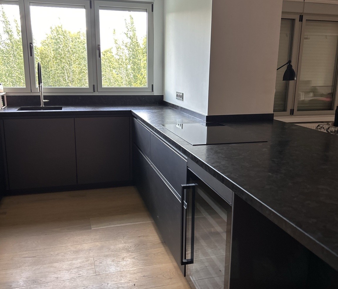 Cocina reformada en tonos oscuros con encimera de piedra y ventana central