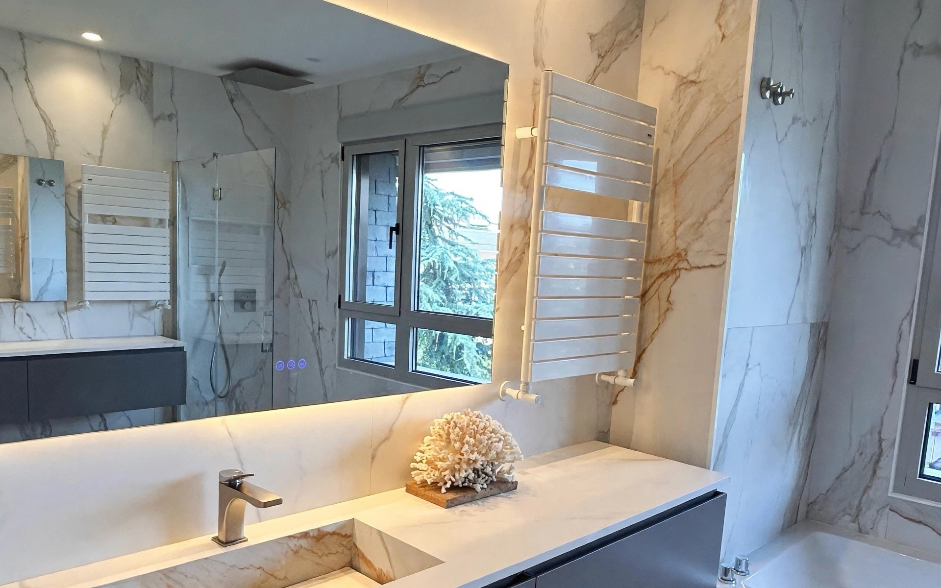 Baño principal en piedra clara con lavabo suspendido e iluminación integrada