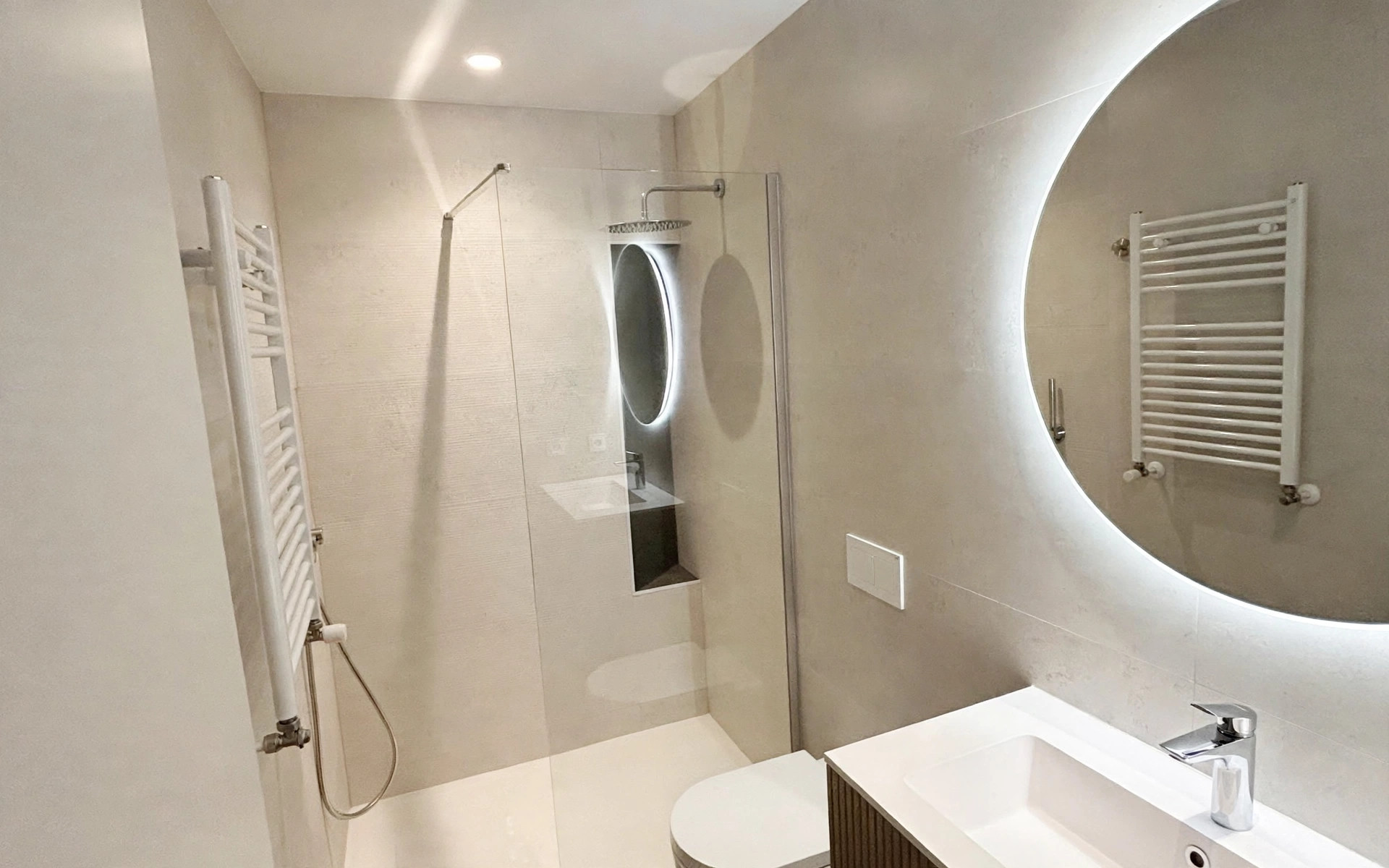 Baño en tonos neutros con espejo circular retroiluminado