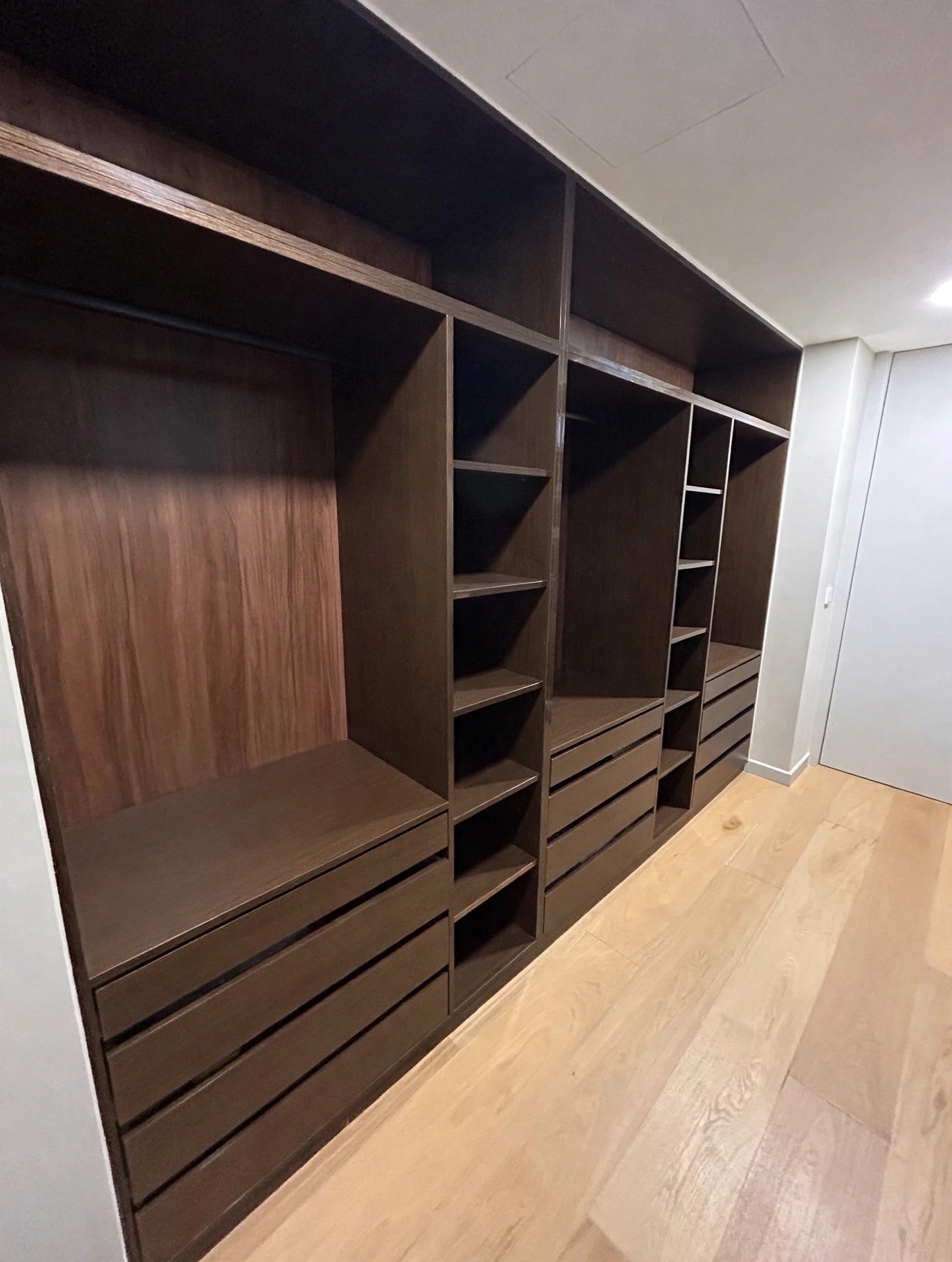 Vestidor vacío de madera oscura con módulos abiertos y cajoneras